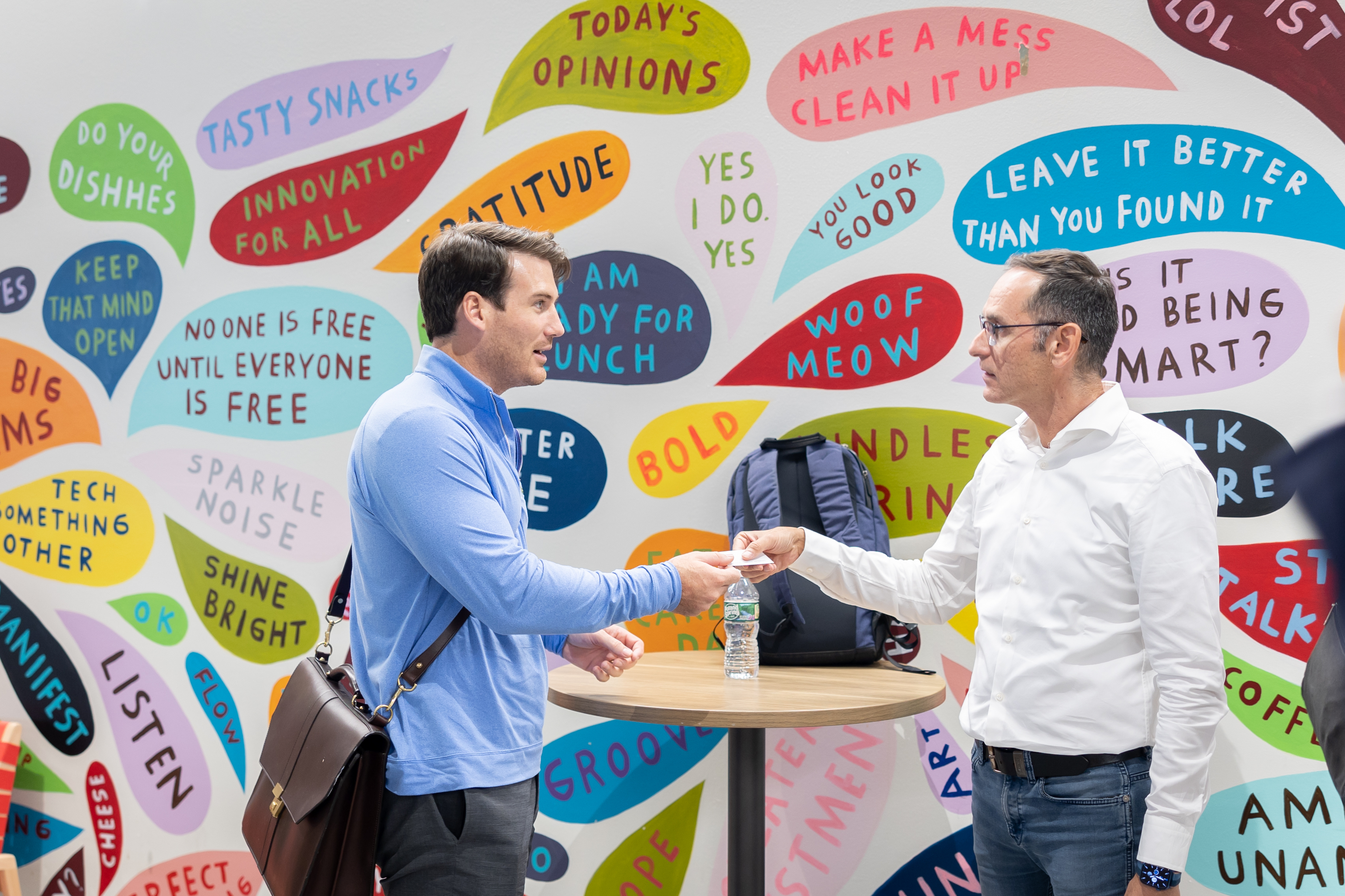 Two men shaking hands in greeting in front of a colorful word wall